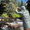 Angler fly fishing for trout by rocks wearing a Rep Your Water Flolite Sun Hoody in spring forest